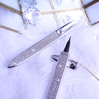 Rhinestone-encrusted self-adhesive eyeliner pens with fine tips on a white feather background with crystal accents.