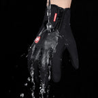 Waterproof black winter sports glove being sprayed with water, featuring a zipper closure and red logo tag.