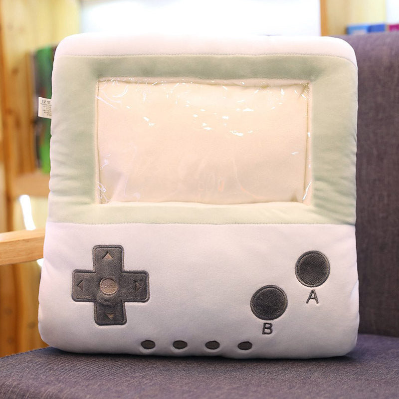 Soft plush pillow shaped like a vintage game console with a clear screen pocket, hand warmer side slots, and buttons.