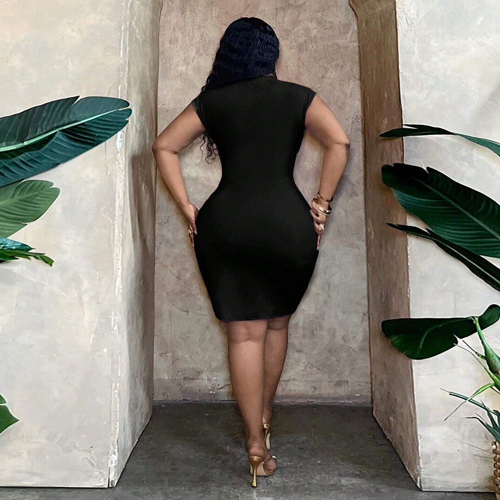 Back view of a woman wearing a fitted black V-neck mini dress with a cinched waist, standing between leafy green plants.