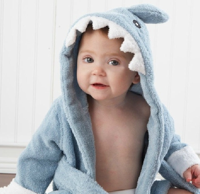 A baby wearing a soft, blue cotton shark-themed hooded bathrobe with white felt teeth detail.