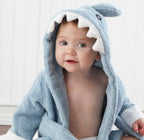 A baby wearing a soft, blue cotton shark-themed hooded bathrobe with white felt teeth detail.