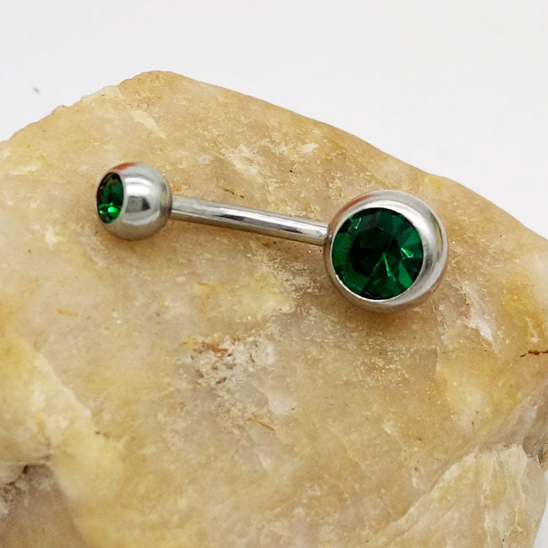 Titanium steel belly ring with two faceted emerald-green gemstones resting on a textured, beige decorative stone.