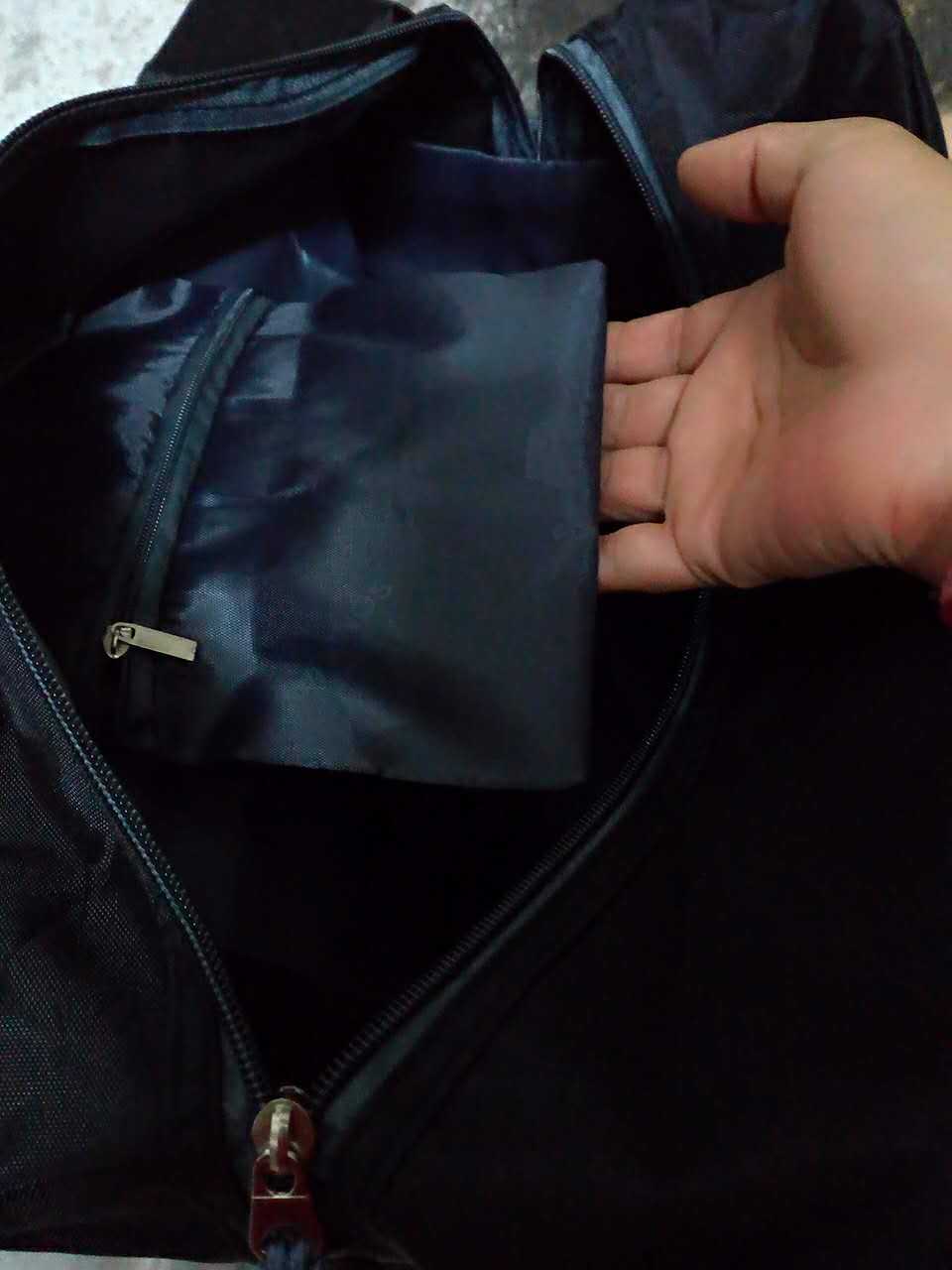 Open black nylon yoga gym bag showing a hand reaching into a zippered interior pocket.