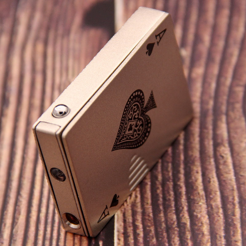 Champagne-colored metal windproof lighter shaped like a playing card with an ace of spades design on a wood background.