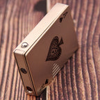 Champagne-colored metal windproof lighter shaped like a playing card with an ace of spades design on a wood background.
