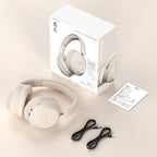 Beige wireless Bluetooth over-ear headphones, matching packaging box, user manual, and two black charging/audio cables.