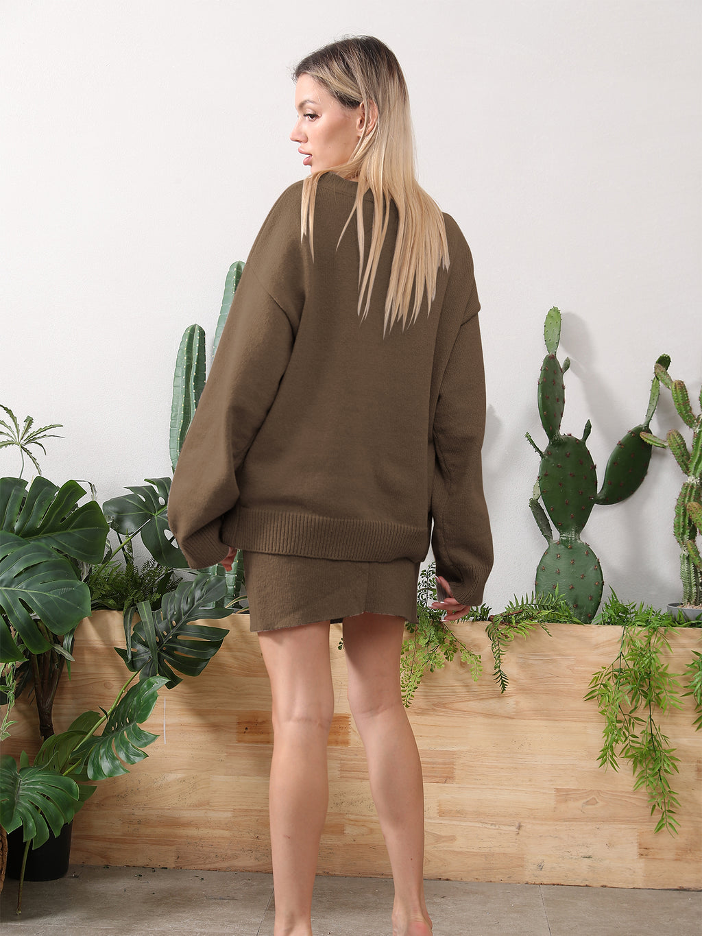 A blonde woman models a cozy brown knit sweater and matching mini skirt set in front of indoor cacti.