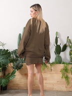 A blonde woman models a cozy brown knit sweater and matching mini skirt set in front of indoor cacti.