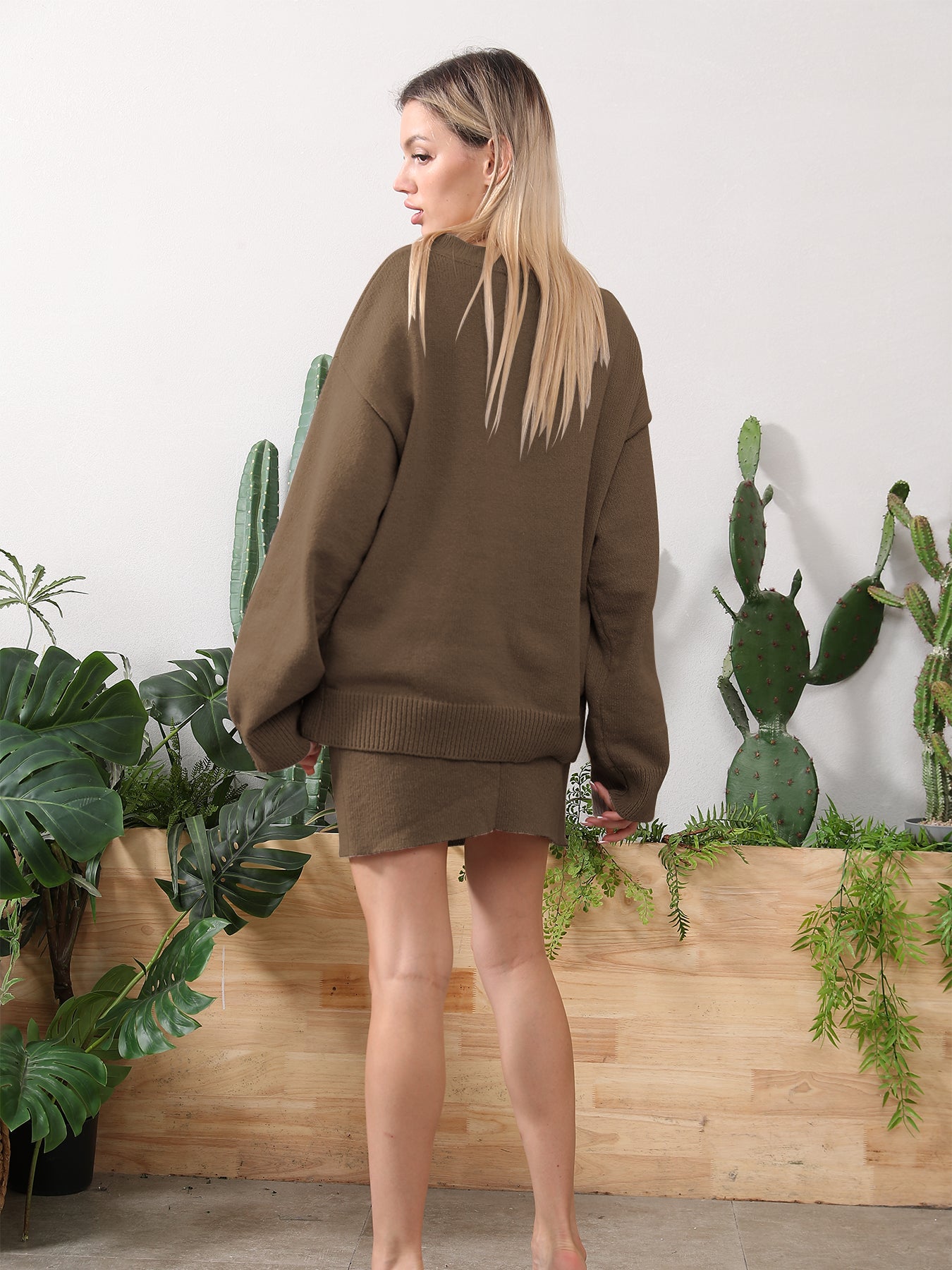 A blonde woman models a cozy brown knit sweater and matching mini skirt set in front of indoor cacti.