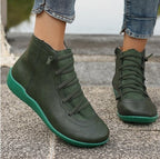 Olive green flat ankle boots with lace-up fronts, side zippers, and matching green soles worn with cuffed jeans.