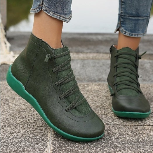 Olive green flat ankle boots with lace-up fronts, side zippers, and matching green soles worn with cuffed jeans.