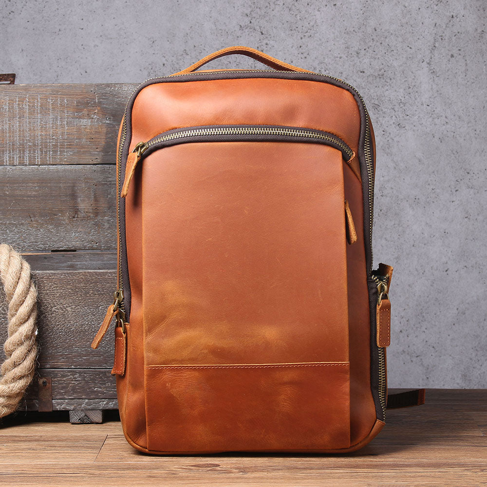 Tan leather vintage-style backpack with bronze zippers, a top handle, and a slim, minimalist silhouette.