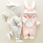 Two soft baby rompers in grey and pink with bunny-ear hoods and white trim, featuring cute chest detail.