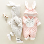 Two baby jumpsuits in gray and pink with bunny-ear hoods, front snaps, and Totoro-style chest patch. Soft cotton blend.