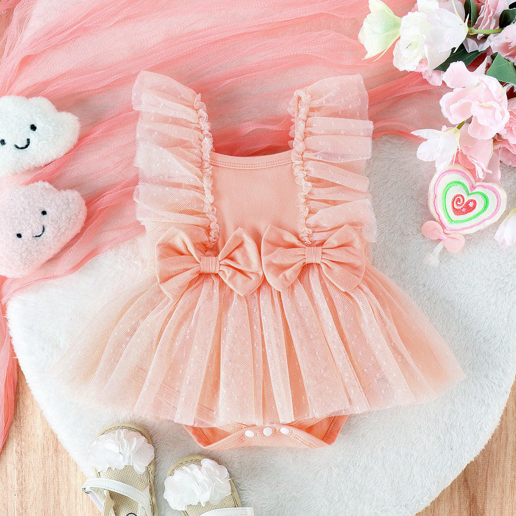 Peach baby romper with tulle ruffles, twin bows, and snap-bottom closure on a white furry background.