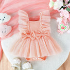 Peach baby romper with tulle ruffles, twin bows, and snap-bottom closure on a white furry background.