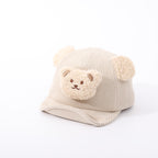 Beige corduroy baby hat with fuzzy bear ears and a cute teddy bear patch on the front, isolated on white.