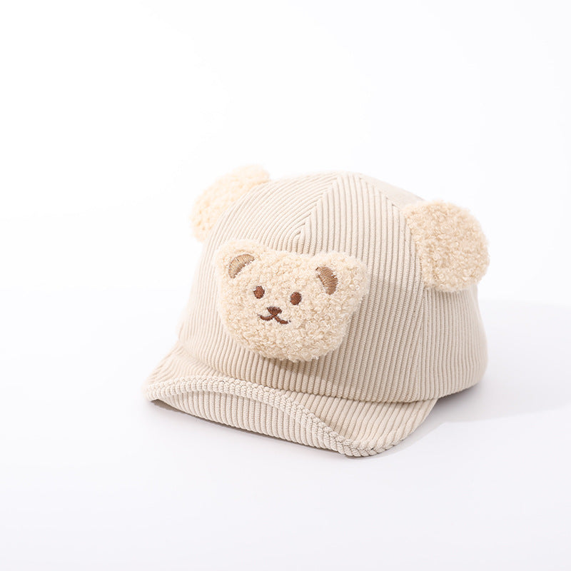 Beige corduroy baby hat with fuzzy bear ears and a cute teddy bear patch on the front, isolated on white.