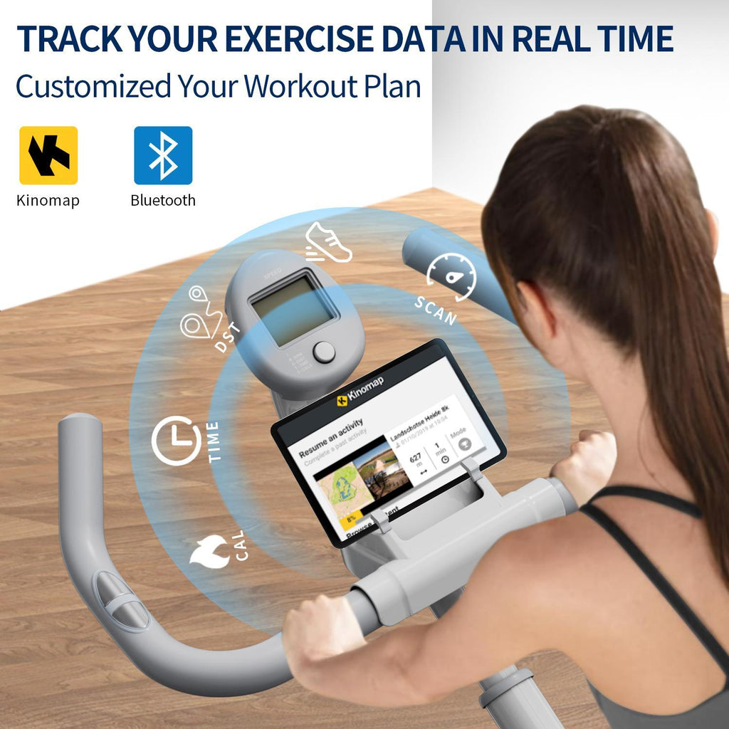 Woman using a stationary exercise bike with a digital display and tablet running the Kinomap fitness app.
