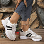 Women's white lace-up sneakers with black stripes, suede accents, and a thick 4cm sole on a wooden floor background.