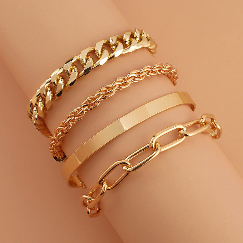 A set of four gold-toned metal bracelets on a wrist, featuring Cuban, rope, bangle, and oval link chain styles.