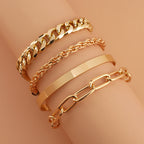 A set of four gold-toned metal bracelets on a wrist, featuring Cuban, rope, bangle, and oval link chain styles.