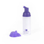 A white pump bottle of V34 purple teeth whitening foam next to a dollop of purple mousse on a white background.