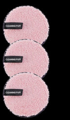 Three round, fluffy, light pink makeup remover puffs with black "CLEANING PUFF" labels against a black background.