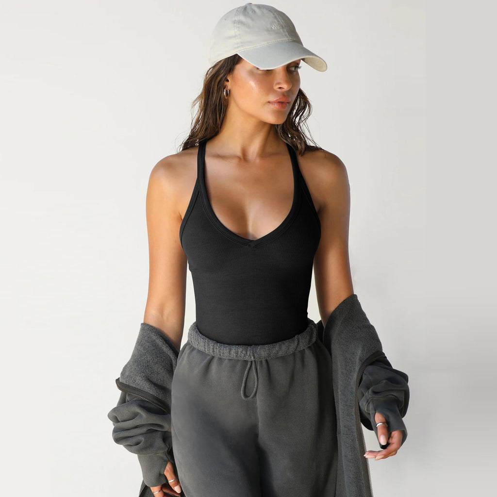 A woman wears a black, ribbed, racerback V-neck knitted tank top with a baseball cap and dark charcoal sweatpants.