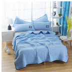 A light blue, quilted cooling blanket on a made bed with matching pillows in a bright, modern bedroom setting.