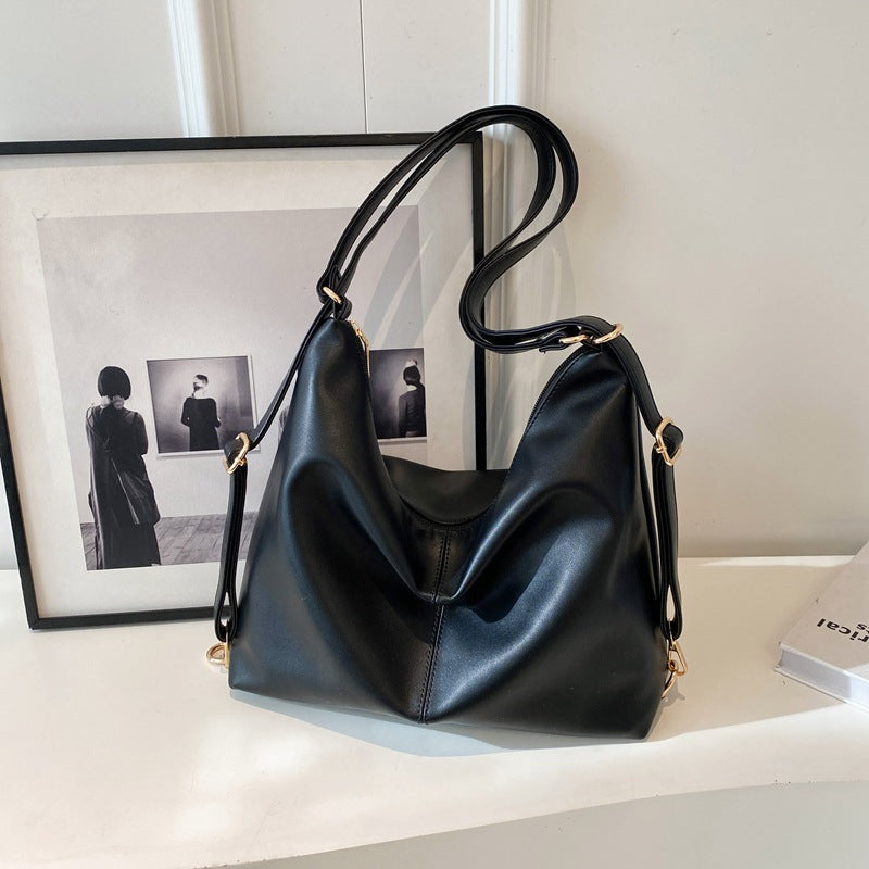 A slouchy black PU leather shoulder bag with gold hardware, featuring a modern, minimalist design on a white surface.