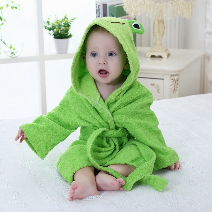 Baby wearing a bright green, hooded cotton bathrobe with cute frog features, sitting on a white bed.
