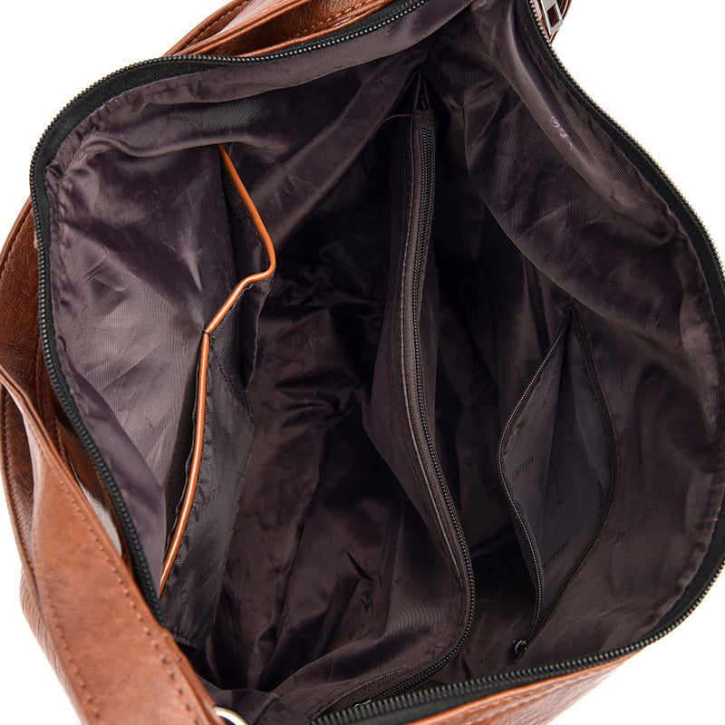 Open brown leather bag showing a dark fabric interior with a central zippered compartment and side organizer pockets.