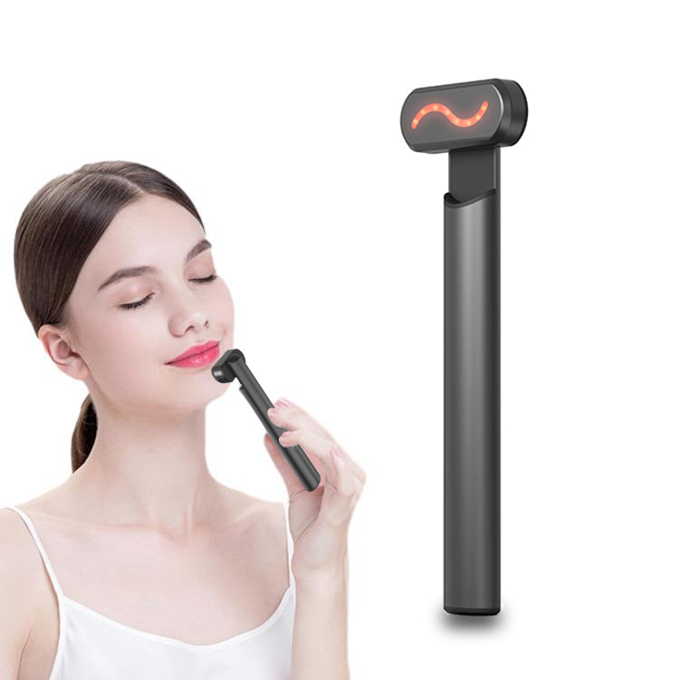 A woman uses a sleek, matte black handheld 4-in-1 facial massager featuring a glowing red LED light therapy head.