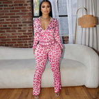 A woman wears a hot pink, leopard-print, high-waisted zip-up jumpsuit with "Glam" embroidery in a chic interior.