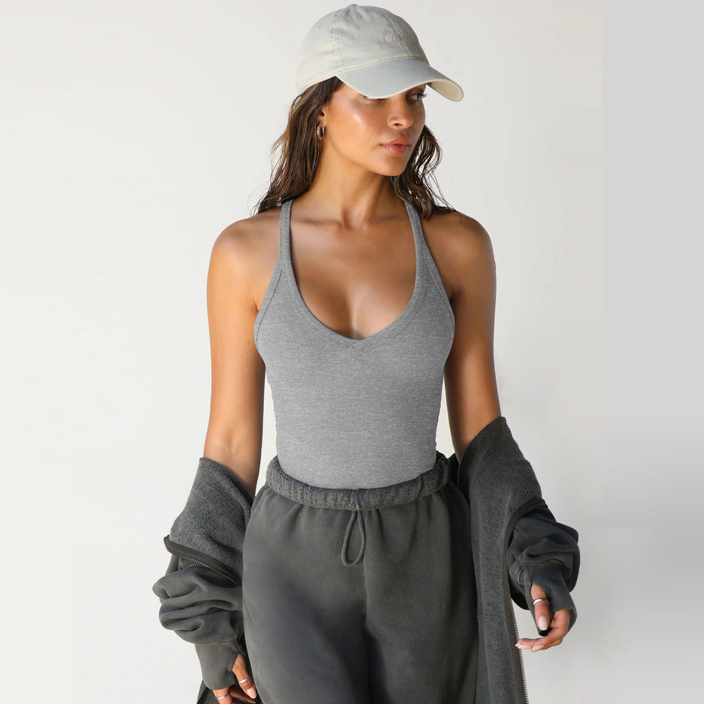 A woman wearing a slim-fit, grey ribbed racerback knit tank top, paired with a cap and dark grey sweatpants.