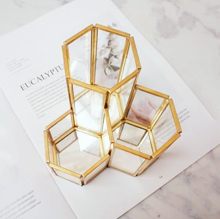 Hexagonal glass and gold metal makeup brush holder with mirrored base, featuring a tiered three-compartment design.