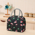 Black waterproof thermal lunch bag with a pink flamingo and leaf print, featuring grey fabric handles and a front pocket.