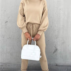 A woman wears a beige long-sleeve fleece sweater set with a drawstring waist, holding a white handbag.