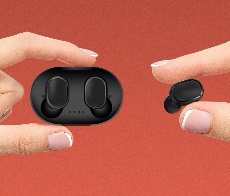 Hands holding a black A6S wireless charging case and one matching matte black in-ear earbud against a red background.