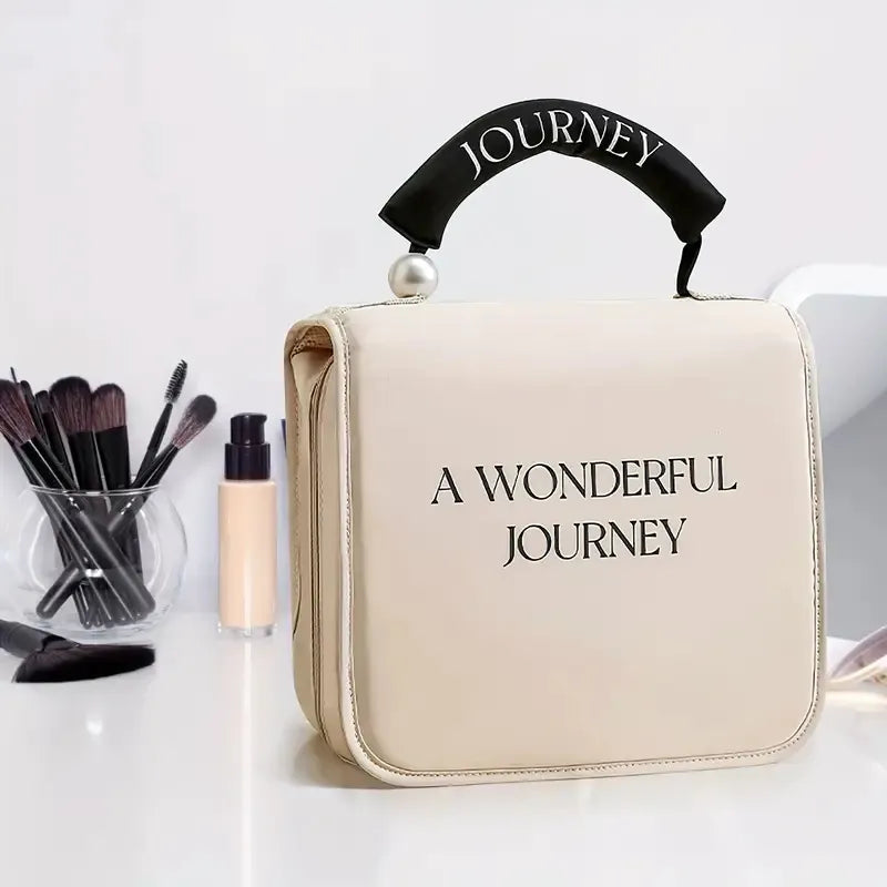Beige cosmetic bag with black handle, pearl accent, and "A WONDERFUL JOURNEY" text on a white surface.