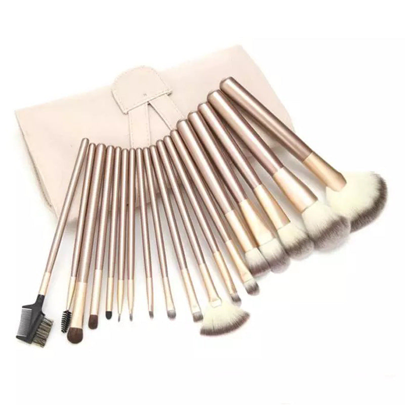 A set of 12 champagne-handled synthetic makeup brushes with creamy white bristles, including a fan brush and case.