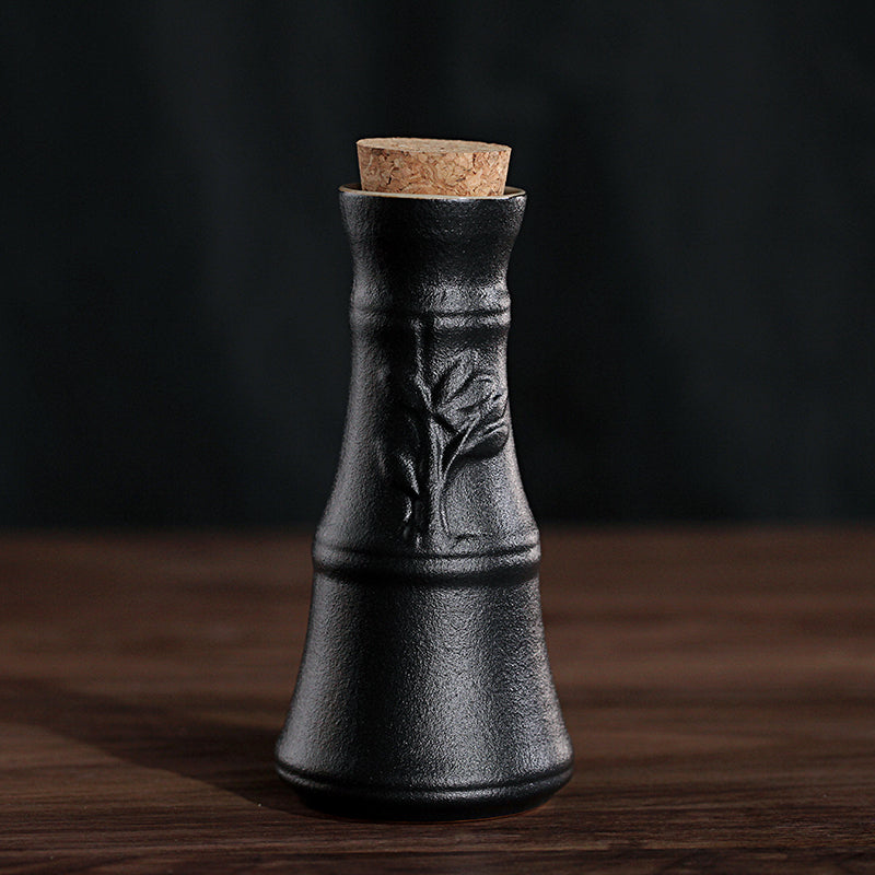 Black textured ceramic wine bottle with an embossed leaf pattern and a cork stopper on a wooden table.