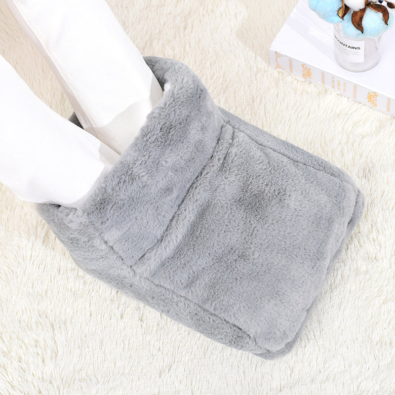 Plush gray electric foot warmer on a white rug, featuring a soft, fuzzy texture with feet inserted inside.