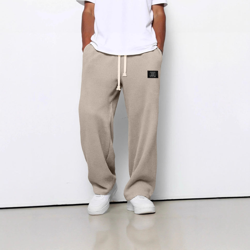 Beige waffle-knit straight-leg trousers with a drawstring waist, side pockets, and a small black patch label.