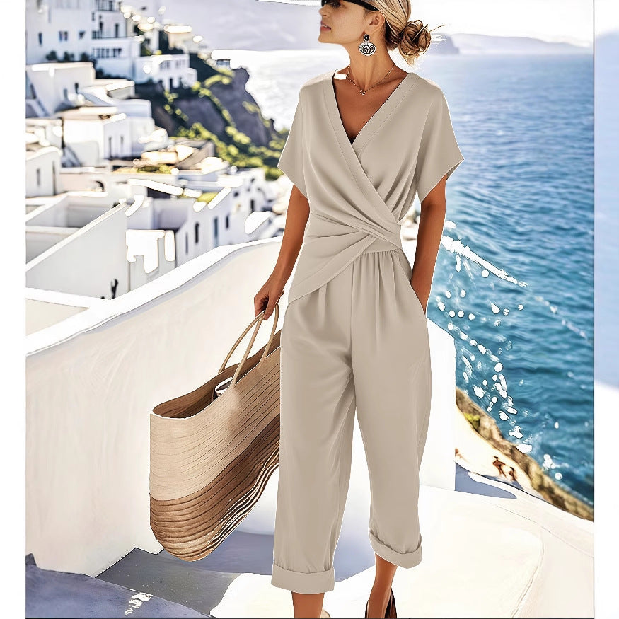 A woman wears a beige, short-sleeve, V-neck, pleated wrap-top jumpsuit with tapered pants while carrying a large tote.