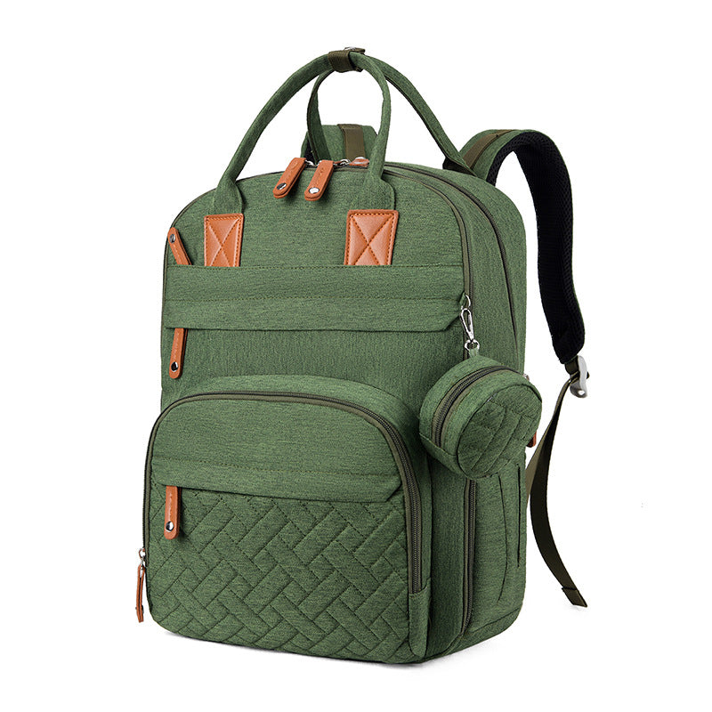 Olive green diaper backpack with tan leather accents, quilted front pocket, top handles, and a small detachable pouch.