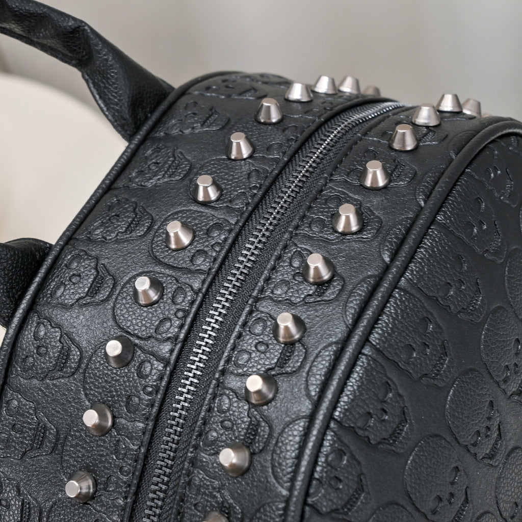 Black leather backpack with embossed skull patterns and silver metal rivet studs along the zipper.
