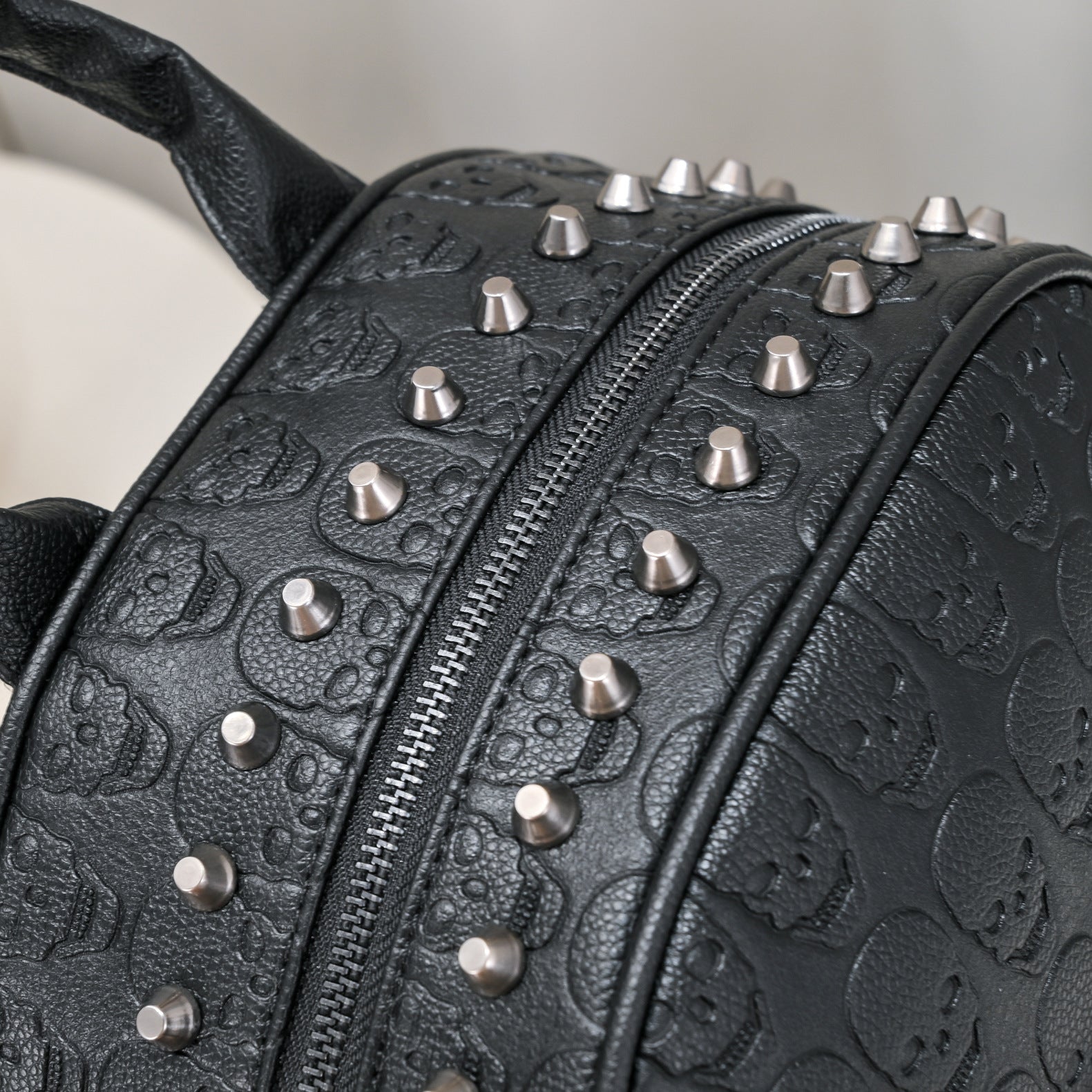 Black leather backpack with embossed skull patterns and silver metal rivet studs along the zipper.